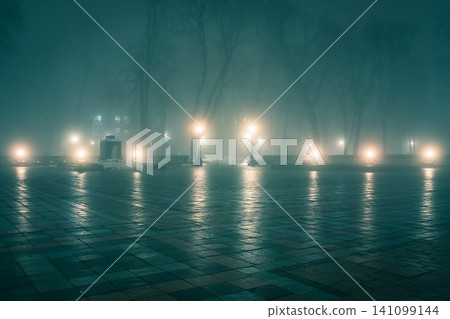 Alley of a night winter park in a fog. Footpath in a fabulous winter city park at night in fog with benches and latterns. Beautiful foggy evening in the Mariinsky Park. Kyiv, Ukraine. Alley of a night winter park in a fog. Footpath in a fabulous winter city park at night in fog with benches and latterns. Beautiful foggy evening in the Mariinsky Park. Kyiv, Ukraine. 141099144