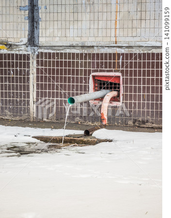 Water flows from the roof of the building through a drainpipe. Early spring and melting snow. 141099159