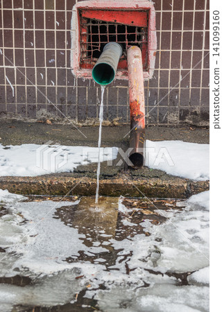 Water flows from the roof of the building through a drainpipe. Early spring and melting snow. Water flows from the roof of the building through a drainpipe. Early spring and melting snow. 141099160