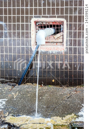 Water flows from the roof of the building through a drainpipe. Early spring and melting snow. Water flows from the roof of the building through a drainpipe. Early spring and melting snow. 141099214
