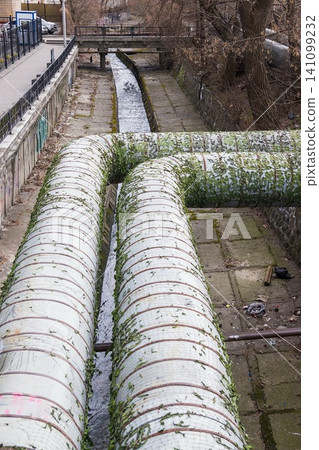 Urban stream. Industrial pipes. Concrete riverbed and river bank 141099232
