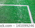 Angle of soccer field with artificial green grass, white lines and light layer of snow. Amateur football field. Sunny spring day 141099246