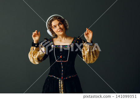 Portrait of a young aristocratic woman with headphones and touching head and dressed in a medieval dress listens music Portrait of a young aristocratic woman with headphones and touching head and dressed in a medieval dress listens music 141099351