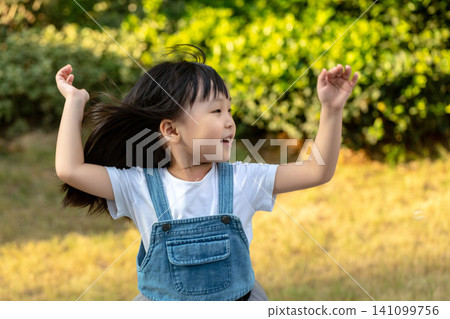 Energetic little Asian girl tossing her hair while playing outdoors in sunlight Energetic little Asian girl tossing her hair while playing outdoors in sunlight 141099756
