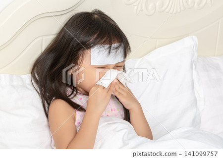 Asian Little Girl Blowing Nose with Tissue While Sick in Bed Asian Little Girl Blowing Nose with Tissue While Sick in Bed 141099757