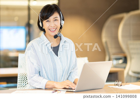 一位微笑的資深女操作員正在使用電腦。 一位微笑的資深女操作員正在使用電腦。 141099808
