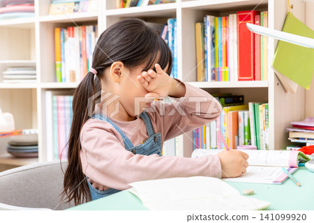 Tired Asian schoolgirl rubbing eyes while doing homework, study fatigue and eye strain concept Tired Asian schoolgirl rubbing eyes while doing homework, study fatigue and eye strain concept 141099920