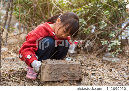 Asian little girl crouched down exploring nature and playing with soil in field Asian little girl crouched down exploring nature and playing with soil in field 141099930