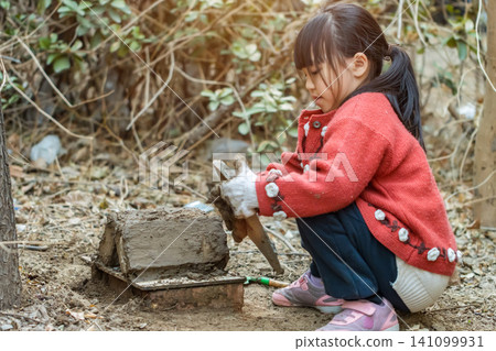 Asian little girl crouched down exploring nature and playing with soil in field Asian little girl crouched down exploring nature and playing with soil in field 141099931