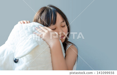 A peaceful young girl resting her head against a soft white fluffy plush toy. 141099938