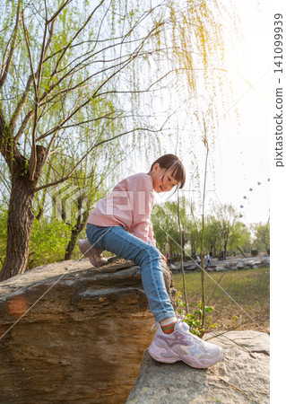 A young girl climbing on a rustic stone wall at an outdoor park. A young girl climbing on a rustic stone wall at an outdoor park. 141099939