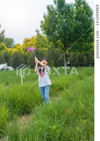 An excited little girl runs through the green grass in the park with a butterfly net. An excited little girl runs through the green grass in the park with a butterfly net. 141099969