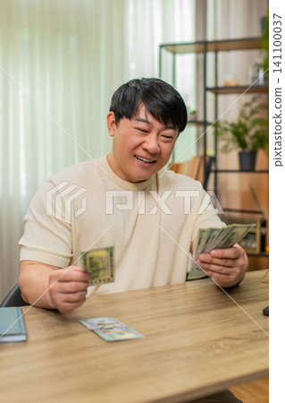 Asian man counting dollars cash, carefully setting some aside, satisfied with smart money management 141100037