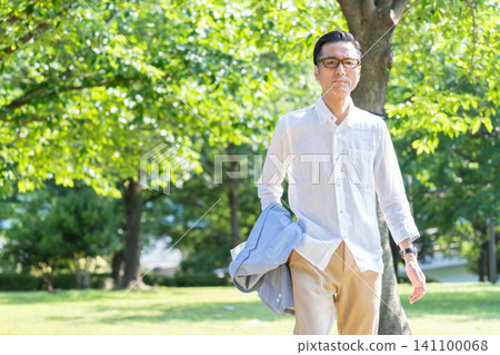 一位戴著眼鏡的老人在綠樹環繞的公園散步。 一位戴著眼鏡的老人在綠樹環繞的公園散步。 141100068