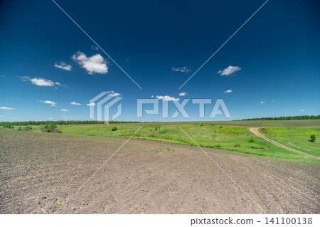 Sunny rural landscape with gravel foreground and green fields under blue sky Sunny rural landscape with gravel foreground and green fields under blue sky 141100138