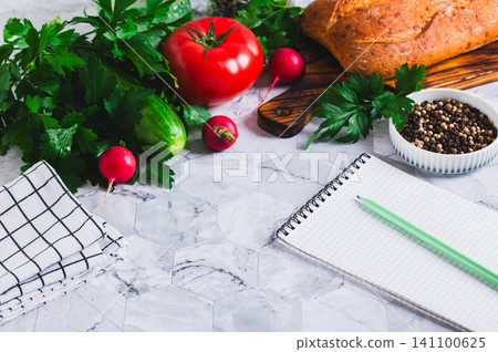 An open notebook and pencil, cucumbers, tomatoes, parsley, bread and spices on the table An open notebook and pencil, cucumbers, tomatoes, parsley, bread and spices on the table 141100625