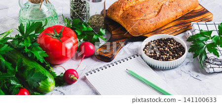 Open recipe notebook, vegetables, herbs and bread on the kitchen table web banner Open recipe notebook, vegetables, herbs and bread on the kitchen table web banner 141100633