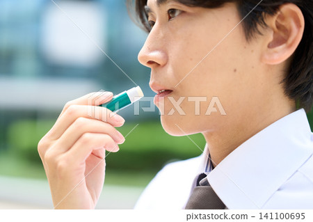 A businessman applying lip balm to his lips. A businessman applying lip balm to his lips. 141100695