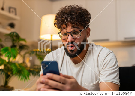 Arabian man amazed by good news on smartphone joyful shock reads message about win smiles with joy Arabian man amazed by good news on smartphone joyful shock reads message about win smiles with joy 141100847