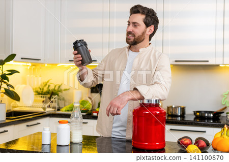 Middle-aged man mixing protein shake in kitchen smiling for fitness diet nutrition workout at home Middle-aged man mixing protein shake in kitchen smiling for fitness diet nutrition workout at home 141100870
