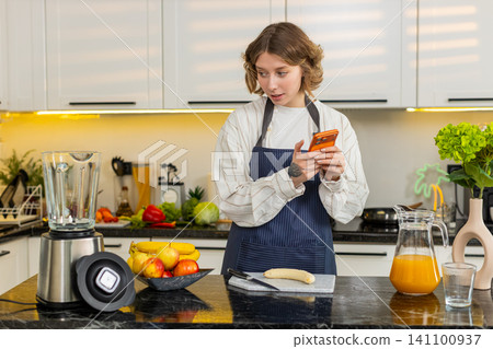 Young woman checking smartphone for food list while preparing healthy diet smoothie in home kitchen Young woman checking smartphone for food list while preparing healthy diet smoothie in home kitchen 141100937