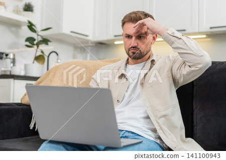 Young man sees defeat on laptop touches forehead sighs and clicks retry after bad news on screen sad Young man sees defeat on laptop touches forehead sighs and clicks retry after bad news on screen sad 141100943