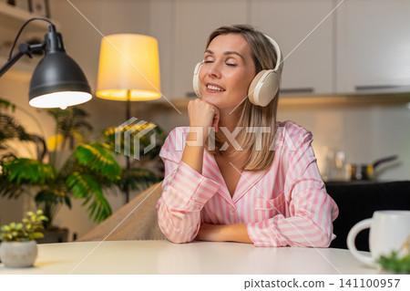 Adult woman in wireless headphones nods to music enjoys chill relax break calm evening vibes tonight Adult woman in wireless headphones nods to music enjoys chill relax break calm evening vibes tonight 141100957