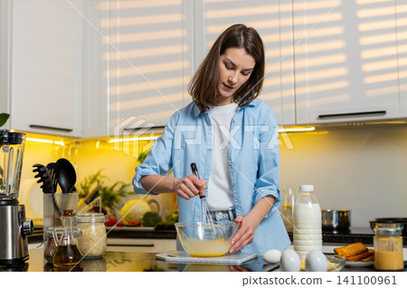 Young woman smiling whisking eggs for omelet in kitchen healthy diet breakfast nutrition routine fit Young woman smiling whisking eggs for omelet in kitchen healthy diet breakfast nutrition routine fit 141100961