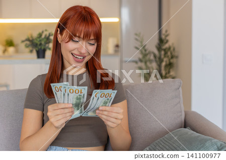 Young woman counts cash dollars with smile happy about salary savings plans invest profit big growth 141100977