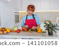Young woman slices cucumber tomato on cutting board makes colorful salad and tastes fresh bite smile 141101058