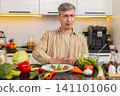 Middle-aged man eating disliked vegetable salad in kitchen during strict diet with strong willpower 141101060