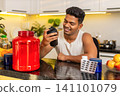 Indian man shaking protein drink in shaker for workout nutrition routine and muscle recovery at home 141101079
