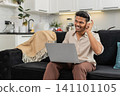 Indian man with wireless headphones edits short video on laptop works freelance smiles with approval 141101105