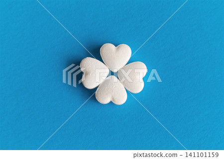 Close-up of four heart-shaped pills arranged in a four-leaf clover shape on a blue fabric background, for topics of heart care, prevention of cardiovascular diseases, and treatment course control. Close-up of four heart-shaped pills arranged in a four-leaf clover shape on a blue fabric background, for topics of heart care, prevention of cardiovascular diseases, and treatment course control. 141101159
