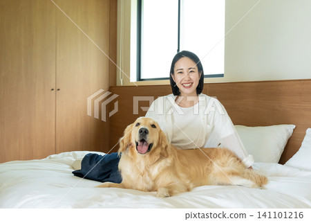 A woman smiles and snuggles up to a golden retriever on a bed. 141101216