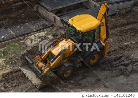 Yellow backhoe loader at muddy construction site near concrete pipes. 141101246