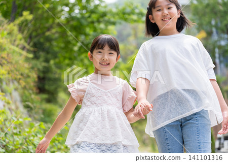 兩個面帶笑容的女孩手牽手散步。 兩個面帶笑容的女孩手牽手散步。 141101316