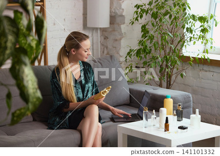 Woman choosing beauty products with laptop in plant filled living room. Woman choosing beauty products with laptop in plant filled living room. 141101332