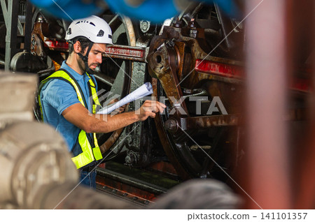 Worker inspects heavy machinery with focused intensity Worker inspects heavy machinery with focused intensity 141101357