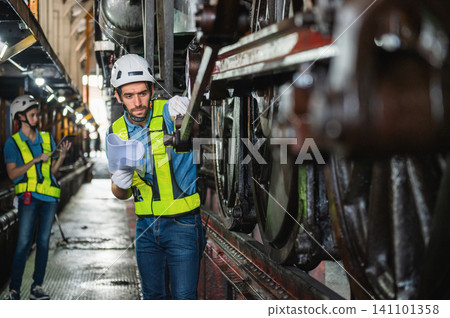 Worker inspects train wheels in dimly lit workshop Worker inspects train wheels in dimly lit workshop 141101358
