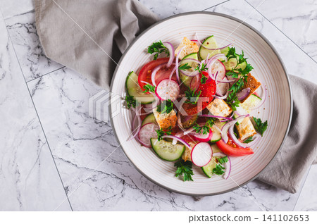 Close up of fresh salad of tomatoes, cucumbers, radishes, onions and croutons on a plate on the table top view Close up of fresh salad of tomatoes, cucumbers, radishes, onions and croutons on a plate on the table top view 141102653