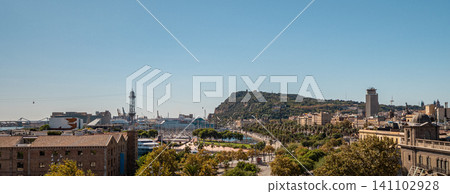 A panoramic view of Barcelona featuring the coastline, hills, and urban architecture under a clear blue sky. The scene captures the vibrant city life and natural beauty. A panoramic view of Barcelona featuring the coastline, hills, and urban architecture under a clear blue sky. The scene captures the vibrant city life and natural beauty. 141102928
