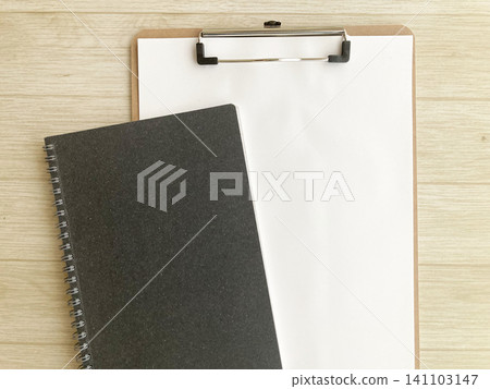A blank clipboard and a black ring notebook are placed on a wood-grain desk, suitable for business or study. A blank clipboard and a black ring notebook are placed on a wood-grain desk, suitable for business or study. 141103147
