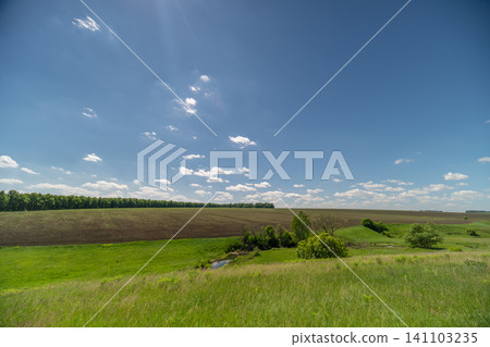 Wide rural field under blue sky with scattered clouds Wide rural field under blue sky with scattered clouds 141103235
