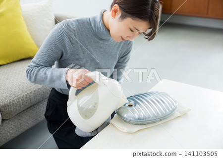 woman using hot water bottle woman using hot water bottle 141103505