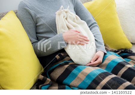 woman using hot water bottle woman using hot water bottle 141103522