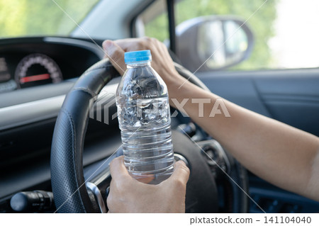 Asian woman driver holding bottle for drink water while driving a car. Plastic hot water bottle cause fire. Asian woman driver holding bottle for drink water while driving a car. Plastic hot water bottle cause fire. 141104040