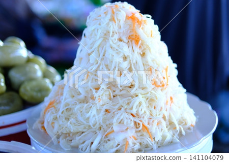 sauerkraut at market. Fresh sauerkraut with carrot shreds displayed in transparent plastic container on market counter, market vendor presenting sauerkraut at market. Fresh sauerkraut with carrot shreds displayed in transparent plastic container on market counter, market vendor presenting 141104079