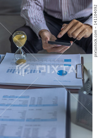Business Consultant Analyzing Data Sheets and Financial Charts at Desk with Hourglass on Table. Time Management Concept. Business Consultant Analyzing Data Sheets and Financial Charts at Desk with Hourglass on Table. Time Management Concept. 141104092