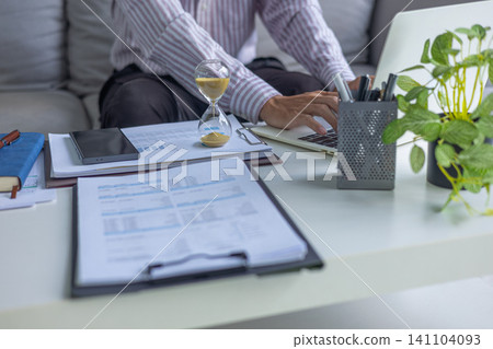 Business Consultant Analyzing Data Sheets and Financial Charts at Desk with Hourglass on Table. Time Management Concept. Business Consultant Analyzing Data Sheets and Financial Charts at Desk with Hourglass on Table. Time Management Concept. 141104093